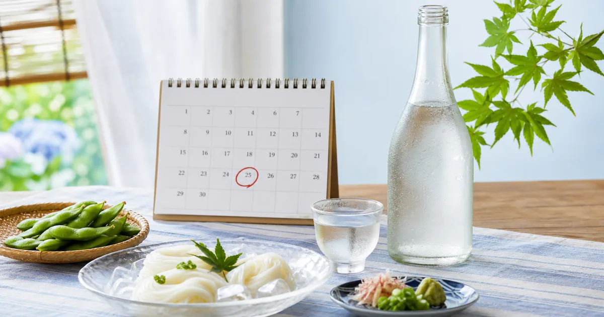 冷えた生酒の瓶と杯、6月25日に印を付けたカレンダー、枝豆とそうめんを並べた初夏の食卓